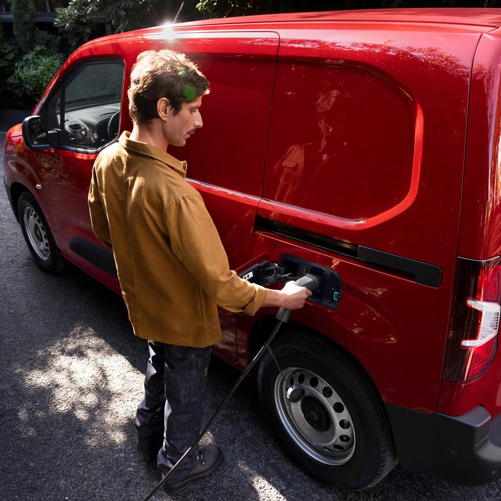 Vista a tre quarti laterale di Citroën ë-Berlingo Van in fase di ricarica, che esprime un design elettrico moderno, praticità quotidiana, connettività e una presenza sicura.