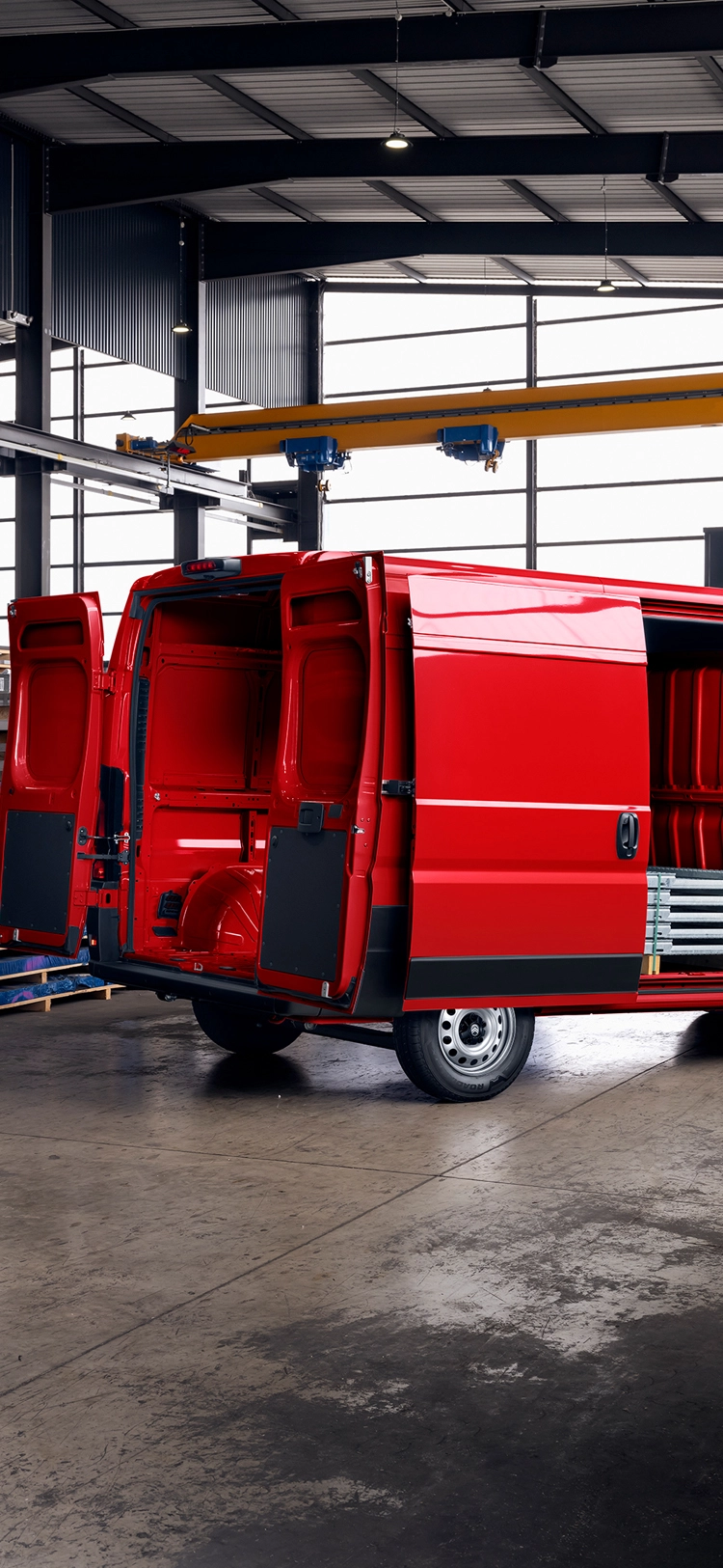 Vista posteriore di tre quarti di Citroën Jumper rossa con le porte del vano di carico aperte all'interno di un magazzino, che mette in risalto l'ampio spazio di carico, la robustezza e la versatilità per il lavoro.