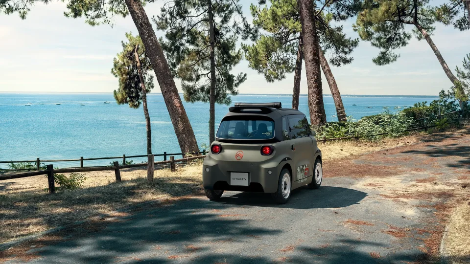 Vista posteriore a tre quarti della Citroën Ami Outdoor sulla costa, una microcar elettrica con tetto aperto per la mobilità nel tempo libero