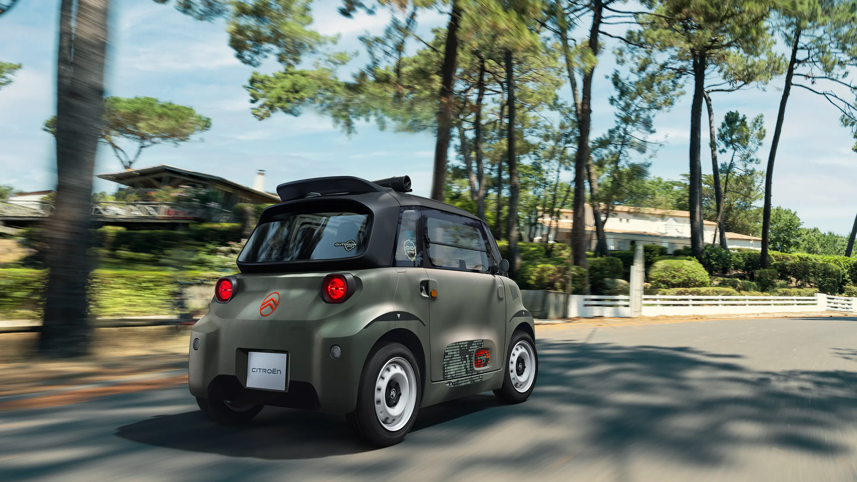 Vista posteriore a tre quarti della Citroën Ami Outdoor con tetto aperto, mentre percorre strade nel bosco