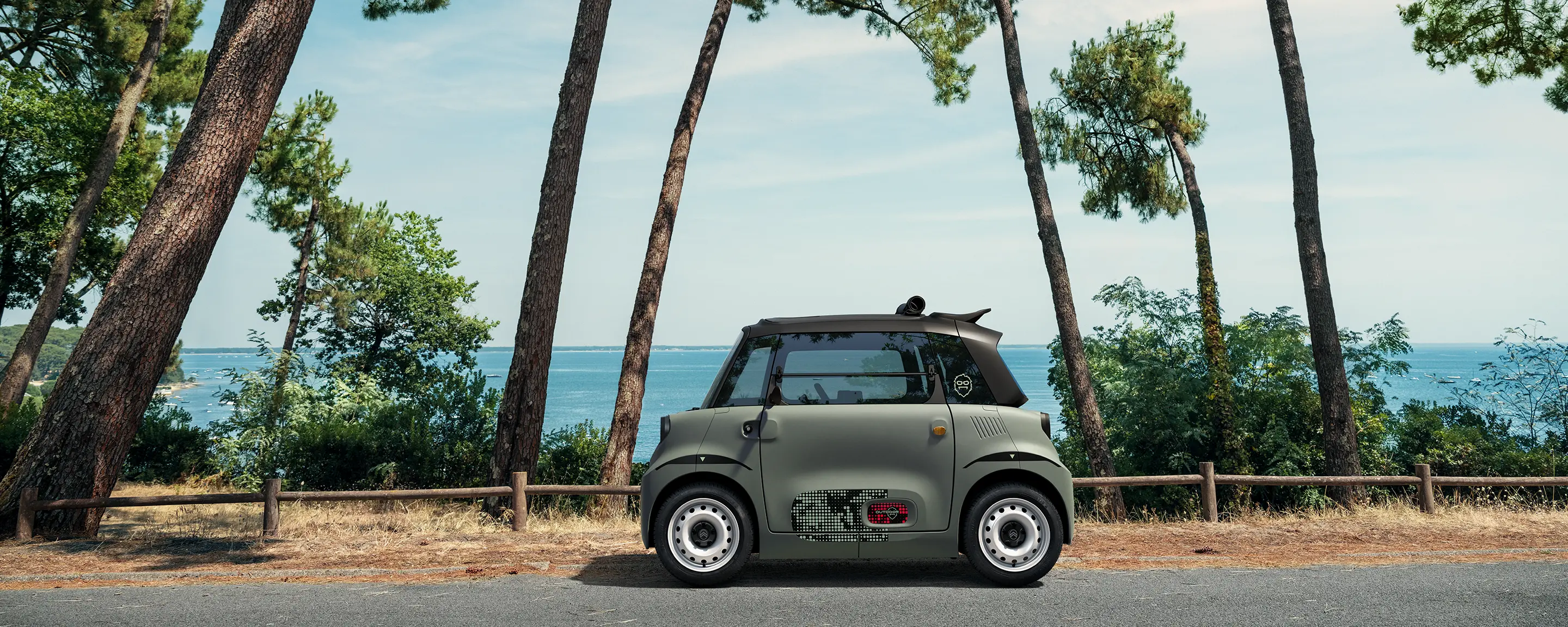 Vista laterale della Citroën Ami Outdoor con tetto apribile, una microcar elettrica ultracompatta in riva al mare