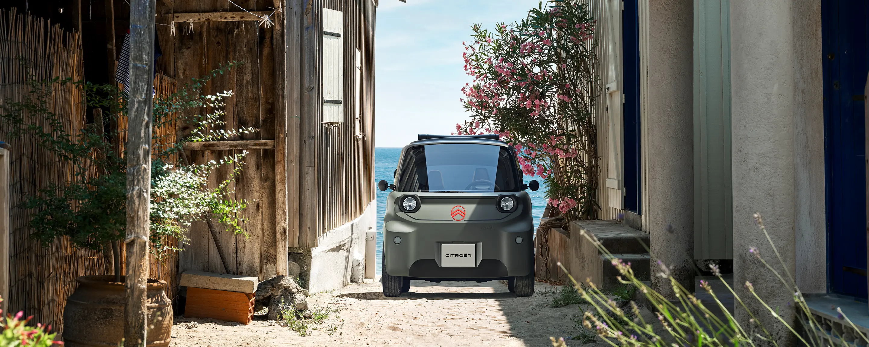 Vista frontale della Citroën Ami Outdoor con fari LED, una microcar elettrica compatta che percorre una stretta strada costiera