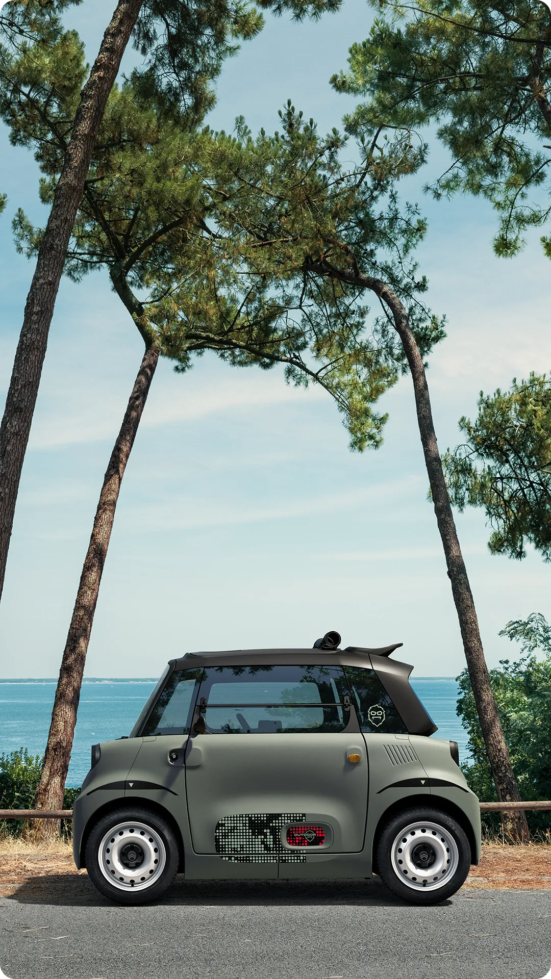 Vista laterale della Citroën Ami Outdoor con tetto aperto, una microcar elettrica sulla costa per la mobilità nel tempo libero