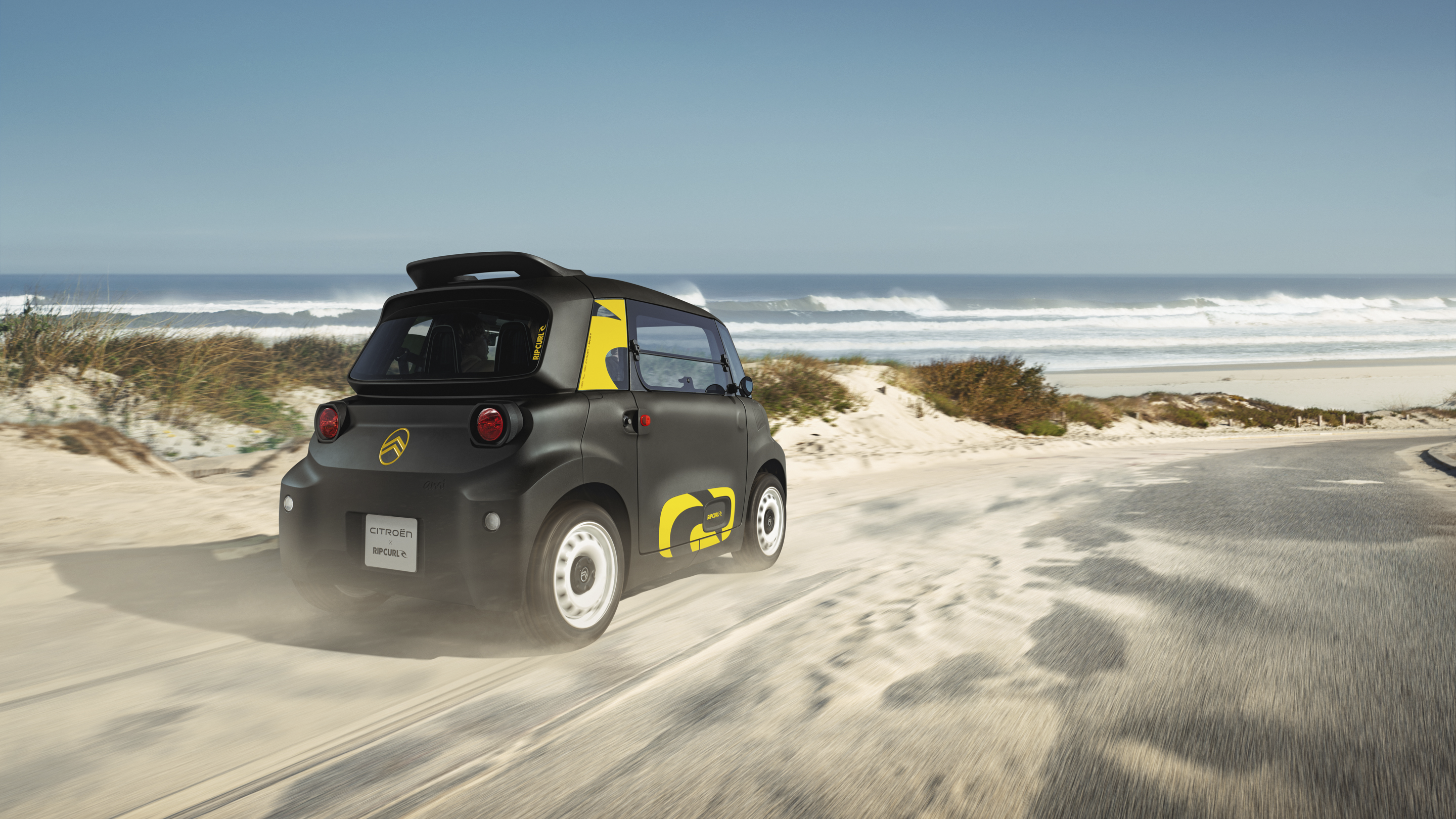 Vista posteriore tre quarti in azione Citroën Ami x Rip Curl elettrica senza patente, Citroën Ami libertà per mobilità urbana elettrica