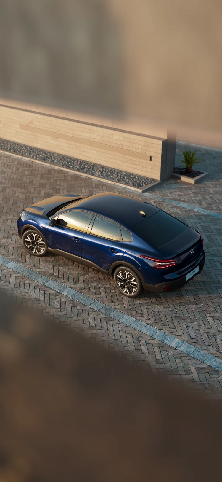 Overhead rear three‑quarter view of the Citroën ë‑C4 X parked on a paved area in sunset lighting