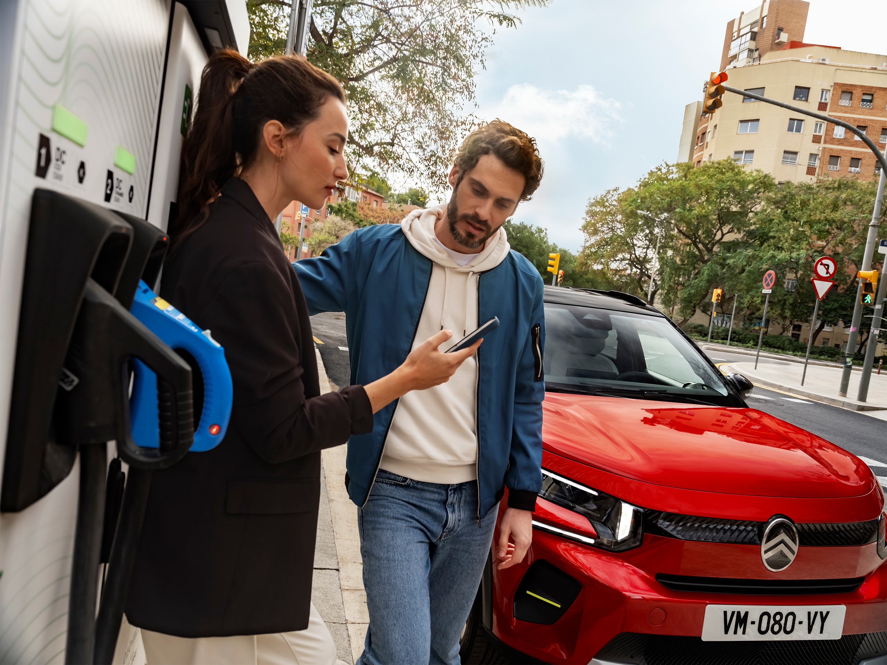 Vista su strada di Citroën ë-C3 durante la ricarica, con persone impegnate nella preparazione della ricarica rapida, per una mobilità urbana efficiente, pratica e accessibile.