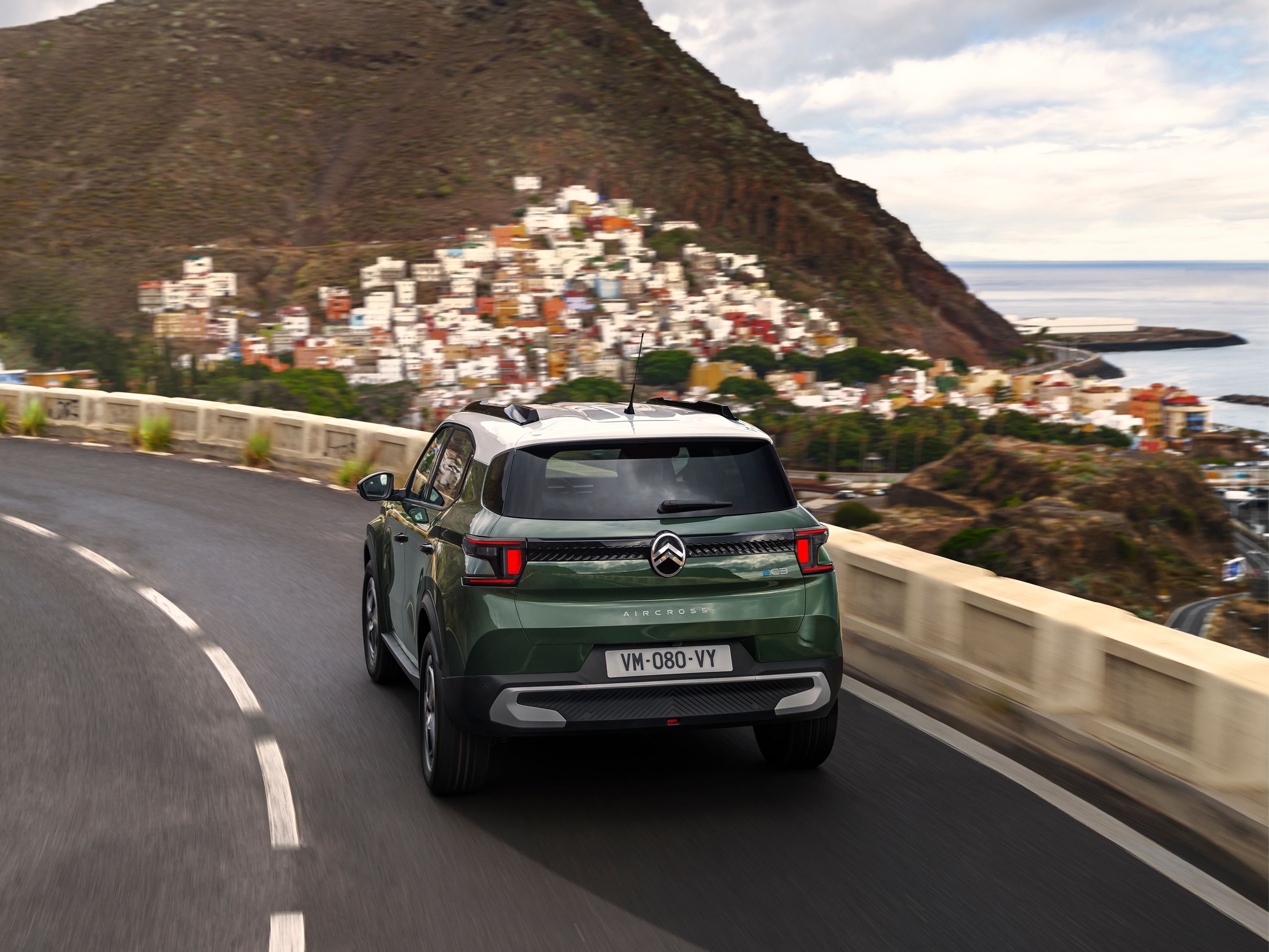 Vista posteriore di tre quarti in movimento di Citroën C3 Aircross su una strada costiera per una mobilità quotidiana fluida, sicura e accessibile.