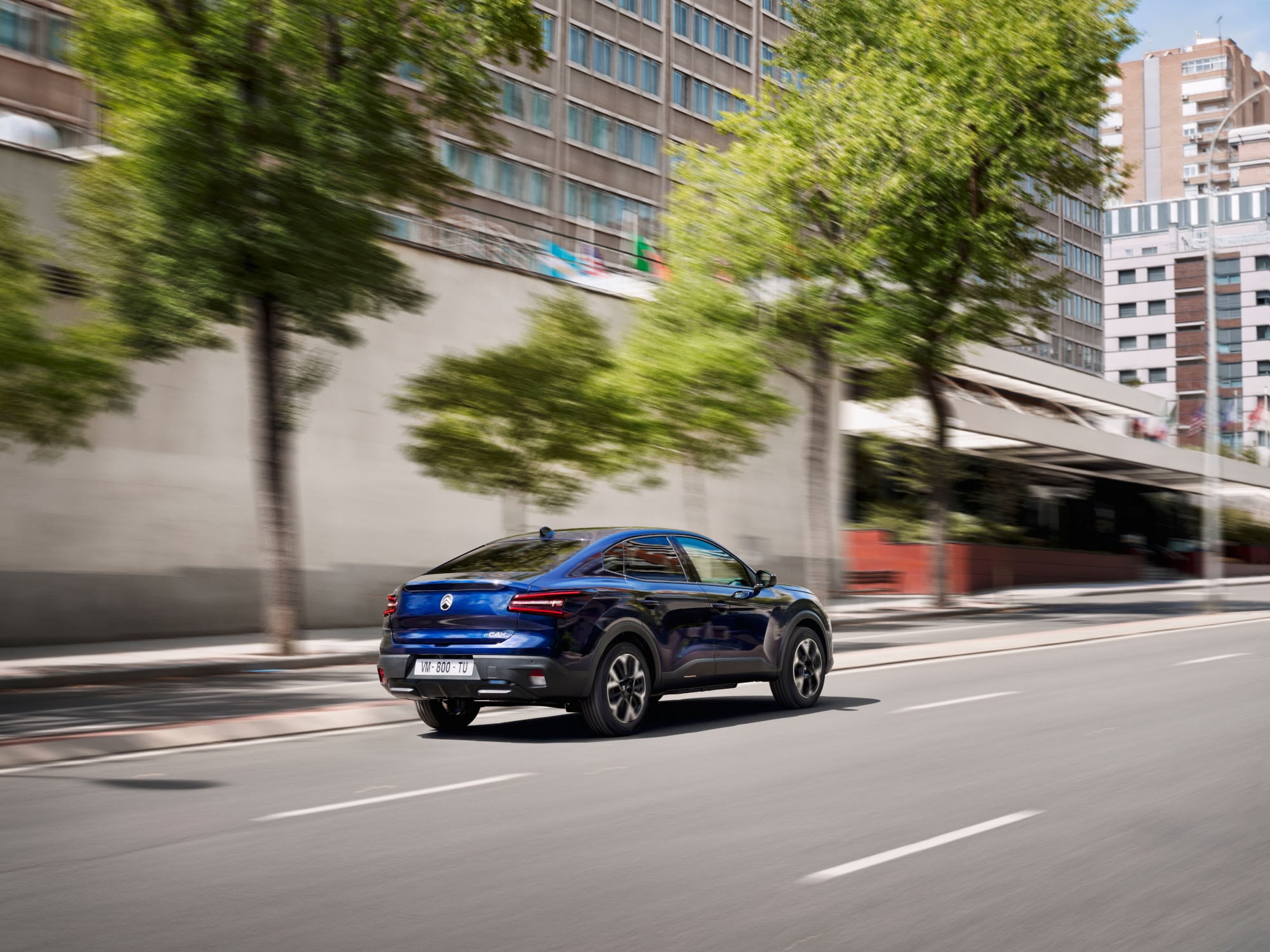 Vista posteriore di tre quarti in movimento della Citroën ë-C4 X che mette in evidenza lo stile fastback moderno per una mobilità efficiente e accessibile