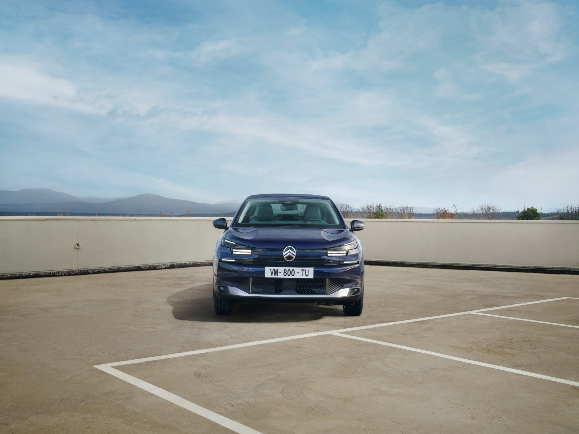Vista frontale della Citroën ë-C4 X in un parcheggio sul tetto, che mette in evidenza il profilo fastback deciso per una mobilità sicura e accessibile