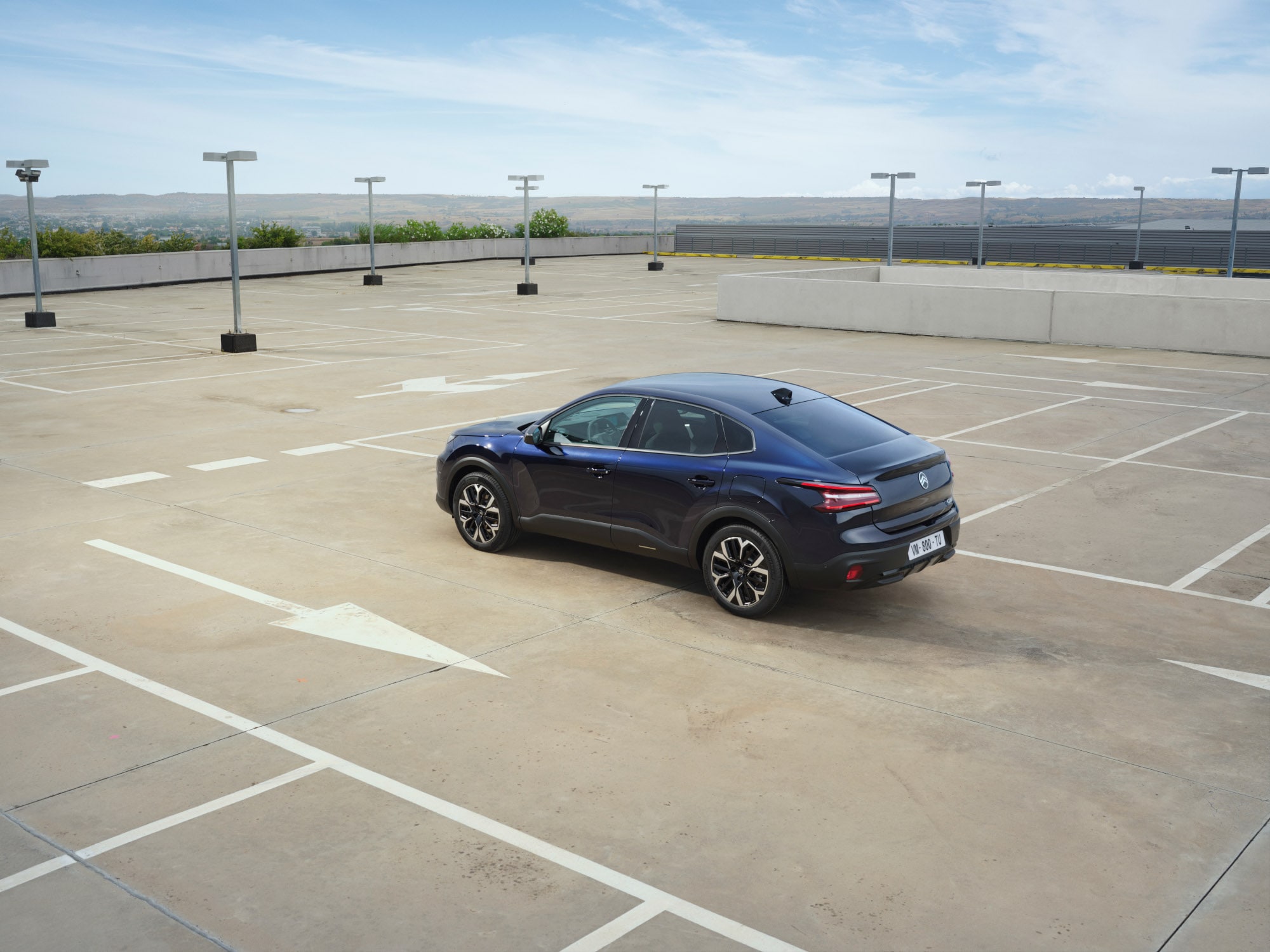 Vista posteriore di tre quarti della Citroën ë-C4 X in un parcheggio sul tetto aperto, che mette in evidenza le linee fastback eleganti per una mobilità accessibile