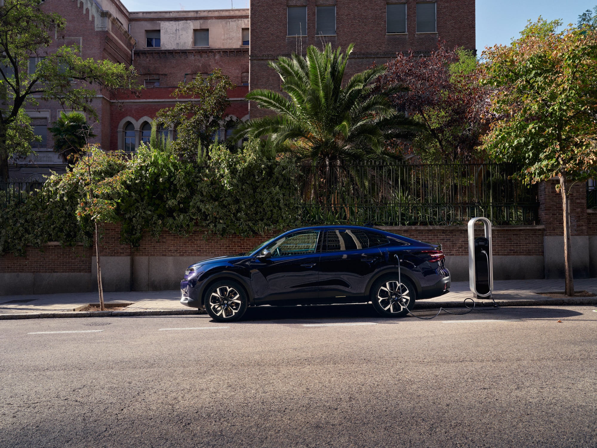 Vista laterale della Citroën ë-C4 X fastback elettrica in ricarica su strada, che mette in evidenza una mobilità urbana comoda e accessibile