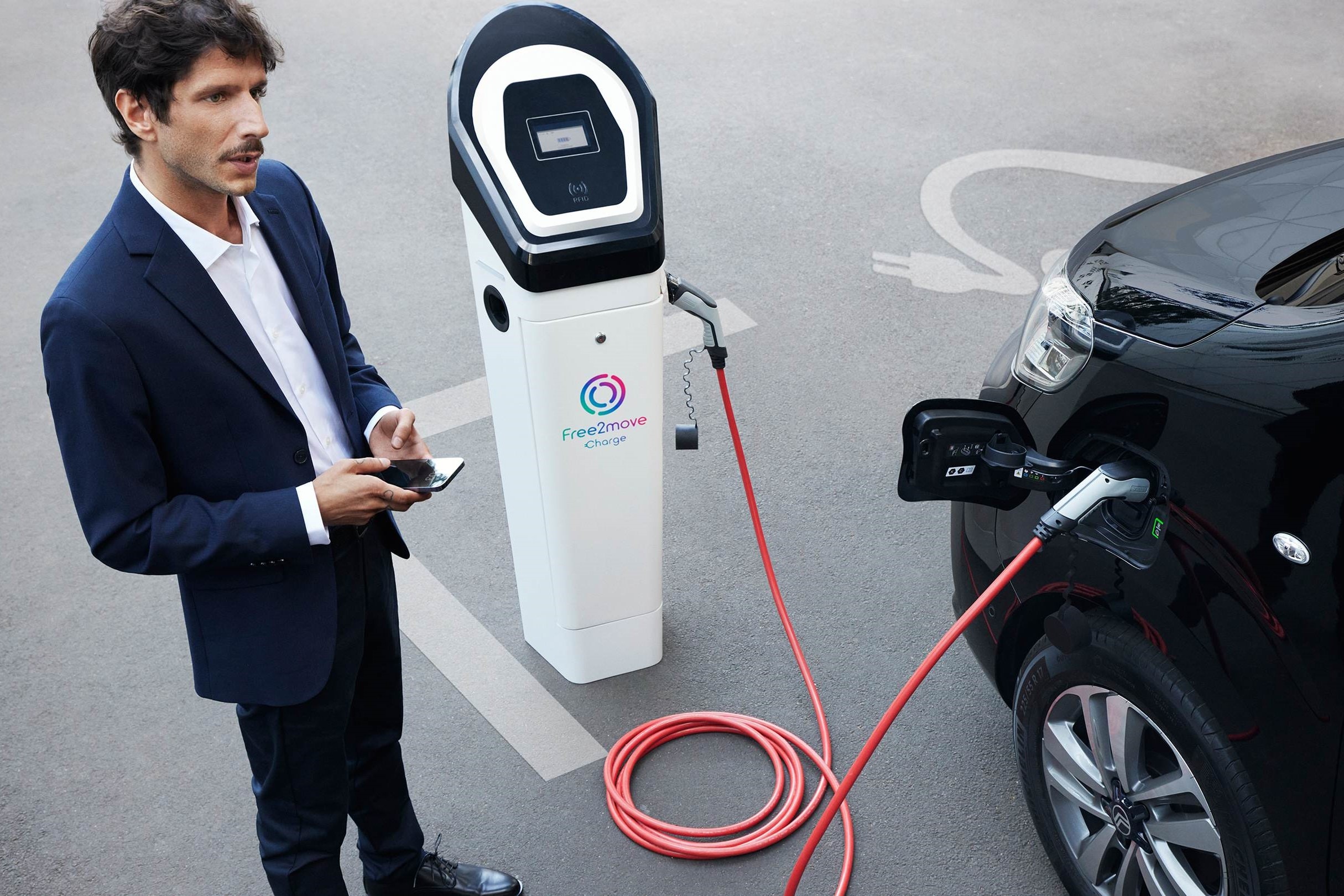 Electric vehicle in ricarica presso una stazione pubblica mentre si utilizza un'app su smartphone per gestire la ricarica con Free2move Charge